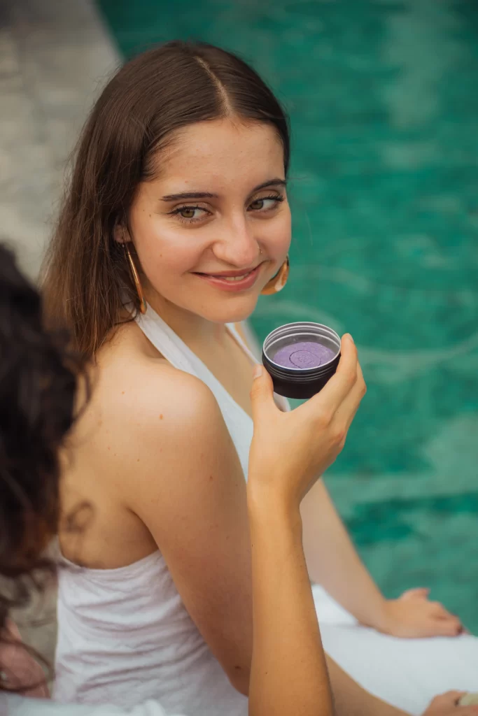 Mujer sonriendo mientras sostiene un envase de producto Rearvora junto al agua