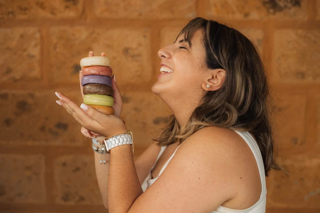 Mujer riendo mientras sostiene una torre de jabones artesanales de colores