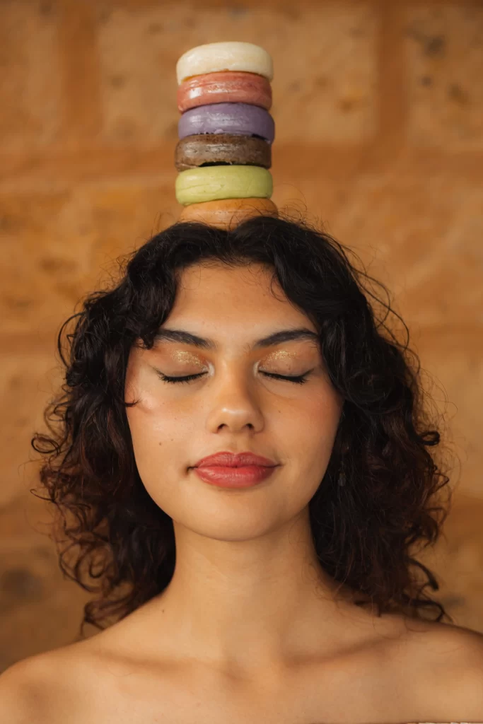 Mujer con los ojos cerrados y una torre de jabones artesanales sobre la cabeza